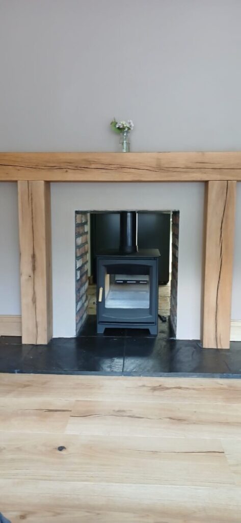 Double-sided Ecosy Hampton stove installation in Parkmill Gower with open door showing interior chamber and rustic brick backdrop by Hopkins Log Burners